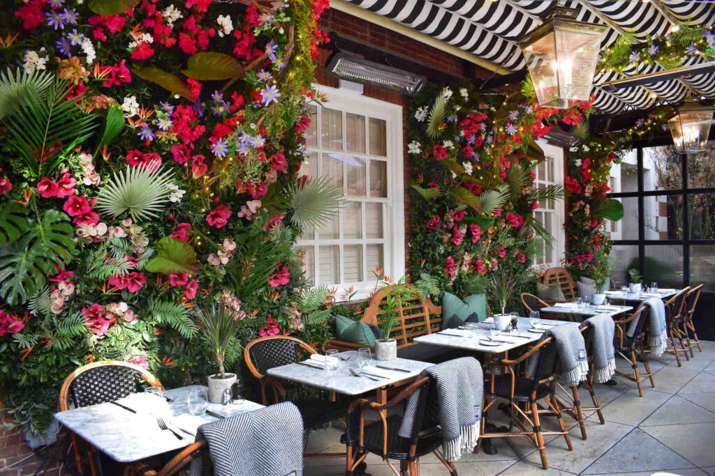 Adorabile ristorante all'aperto con pareti luminose a fiori e coperte sopra le sedie di vimini per mantenere i clienti caldi insieme a un riscaldatore Bromic