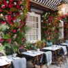 Adorabile ristorante all'aperto con pareti luminose a fiori e coperte sopra le sedie di vimini per mantenere i clienti caldi insieme a un riscaldatore Bromic